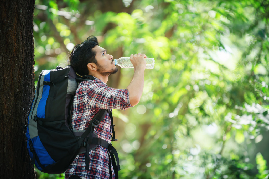 man drinking water from plastic bottle while trekking in a forest